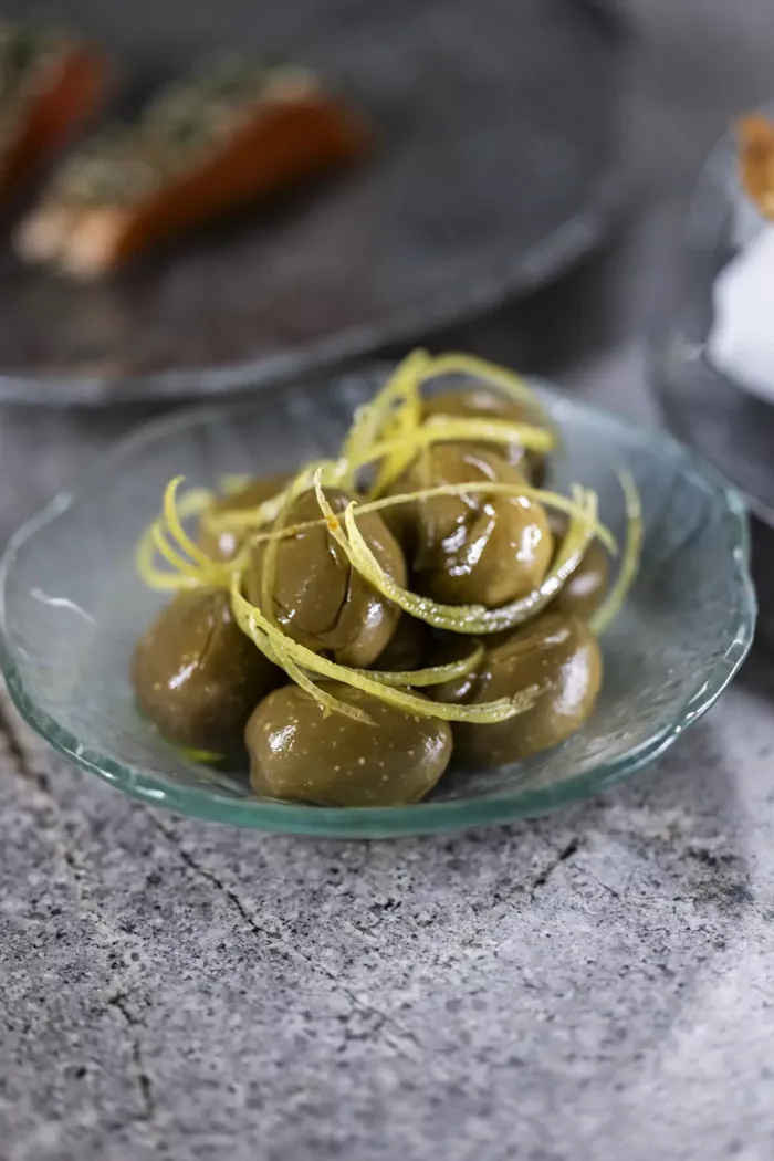 en glasskål fyldt med grønne oliven oven på et bord